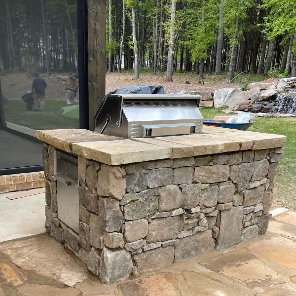 Stone outdoor kitchen with built-in grill and natural stone base.